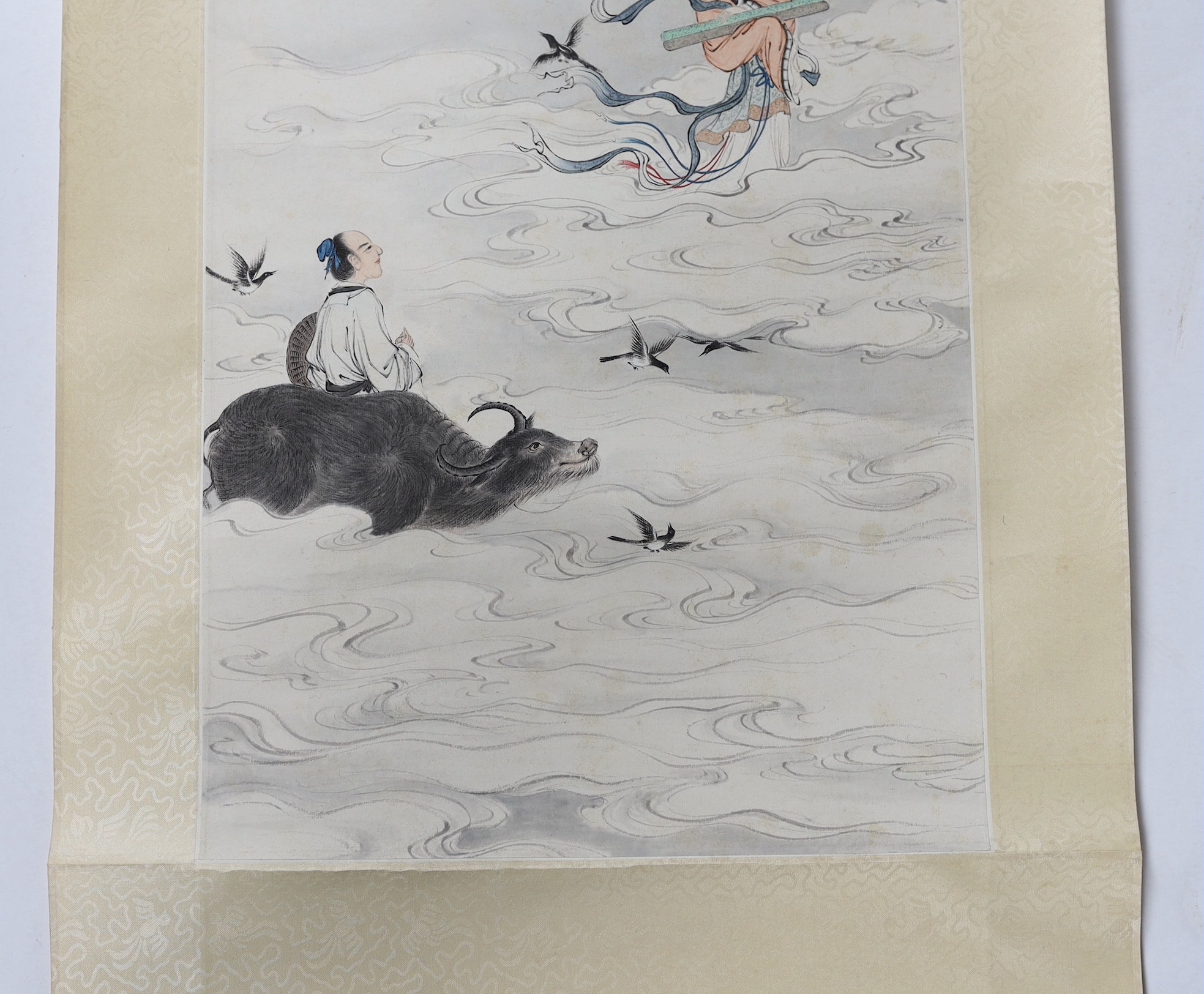 A Chinese scroll painting on paper of a female immortal and a male immortal riding a Buffalo amid clouds and birds, early 20th century, image 77cm x 34.5cm